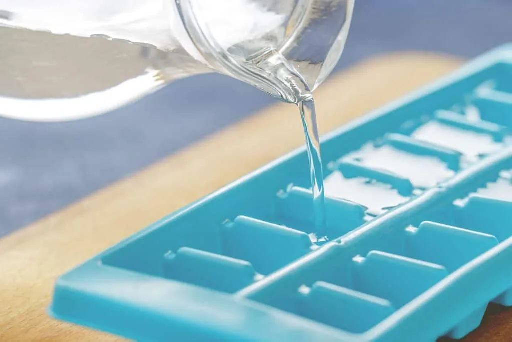 Pouring chicken broth into ice cube tray on the kitchen table